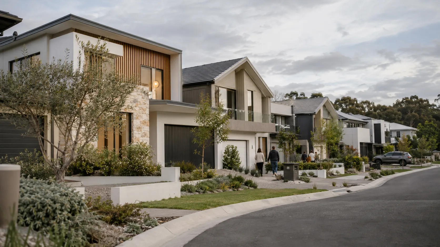 A curving suburban street lined with modern two-storey homes in render, timber and stone, with residents walking along the footpath