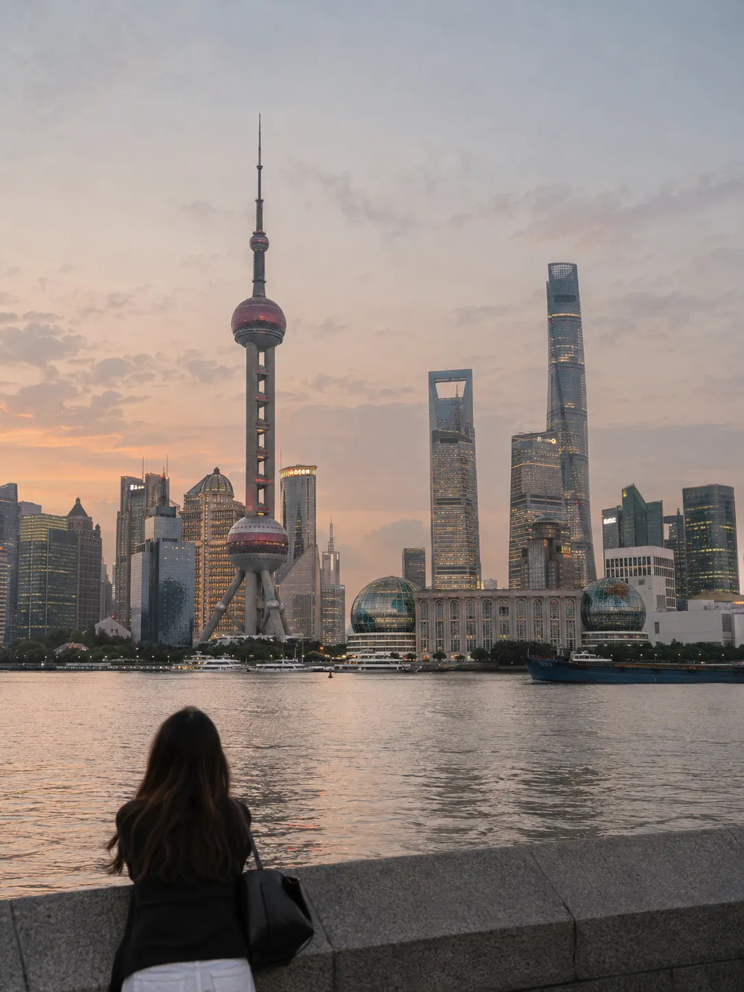 Shanghai’s Pudong skyline at sunset across the Huangpu River, with a woman looking out from the waterfront wall