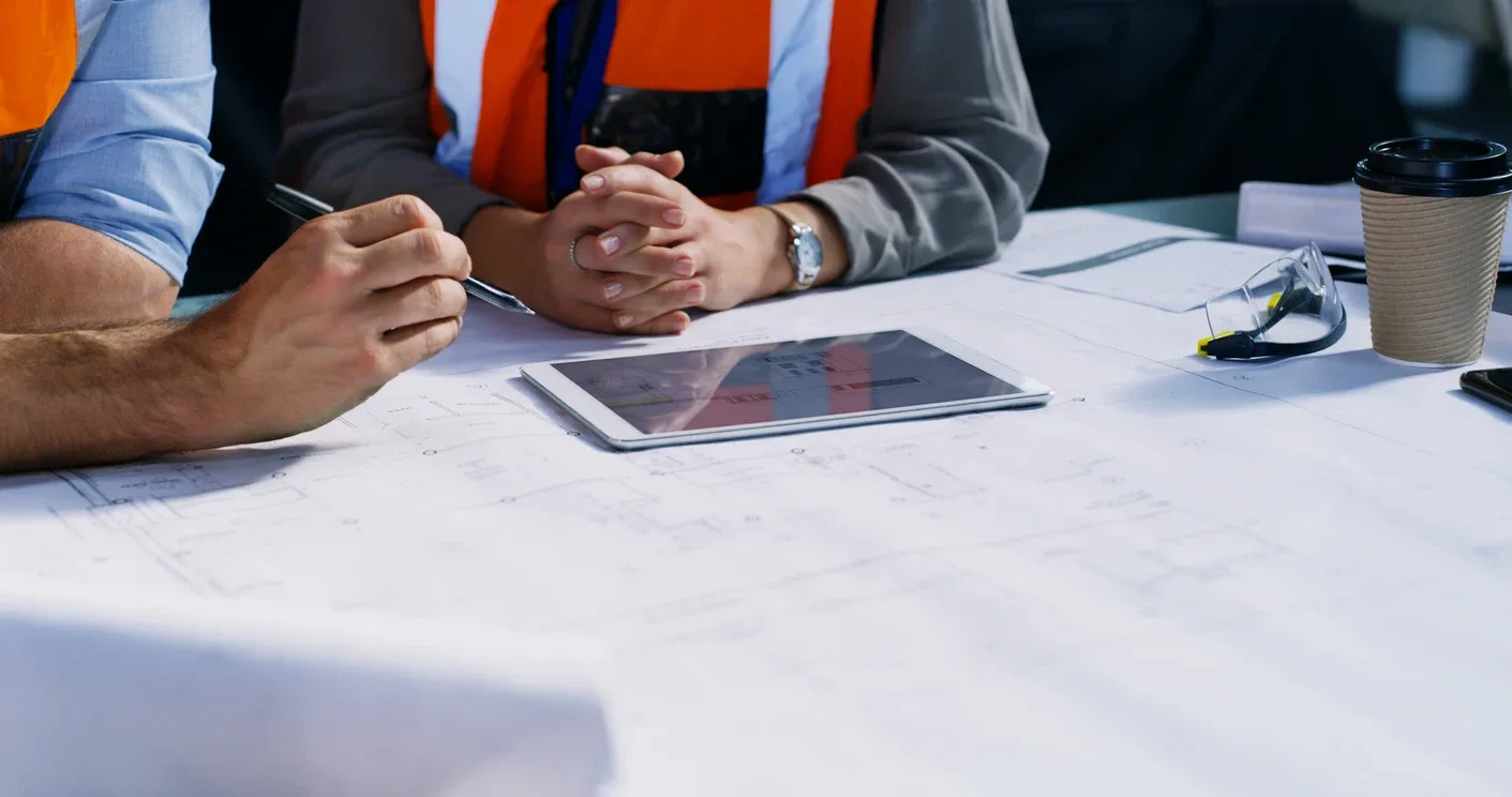 Two people in hi-vis vests reviewing building plans with a tablet