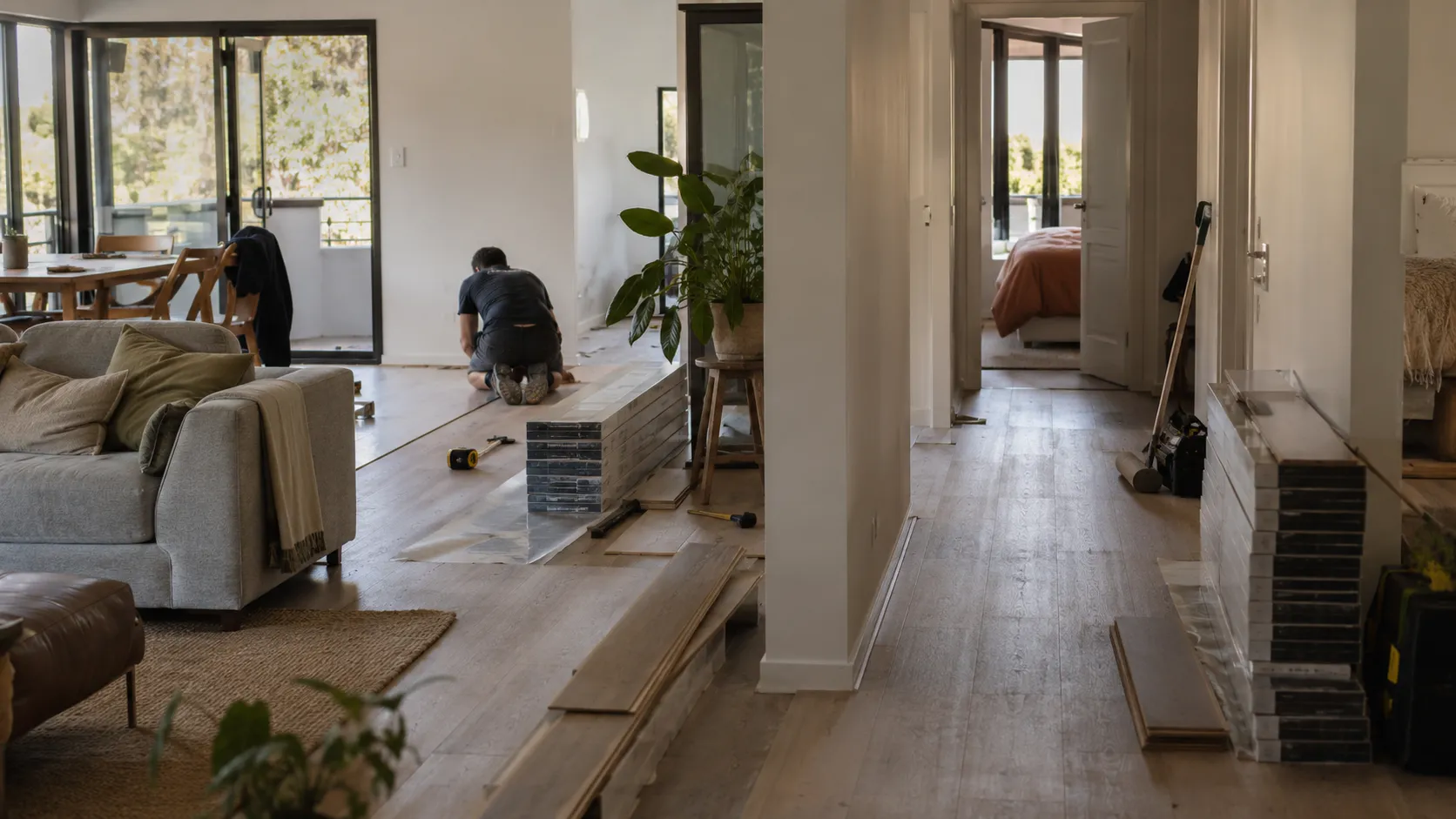 Installers laying timber flooring in an open-plan apartment, with stacked boards and tools scattered across the floor