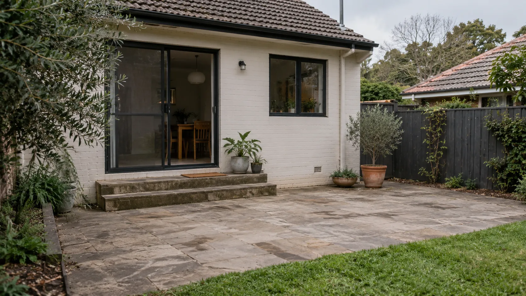 The back of a white-painted brick house with sliding doors opening onto an empty paved terrace
