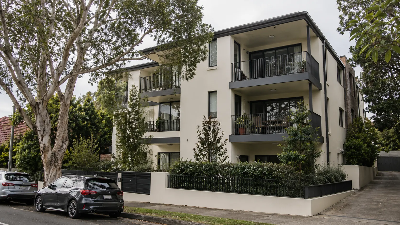 A three-storey cream apartment block with dark balconies behind a rendered front fence