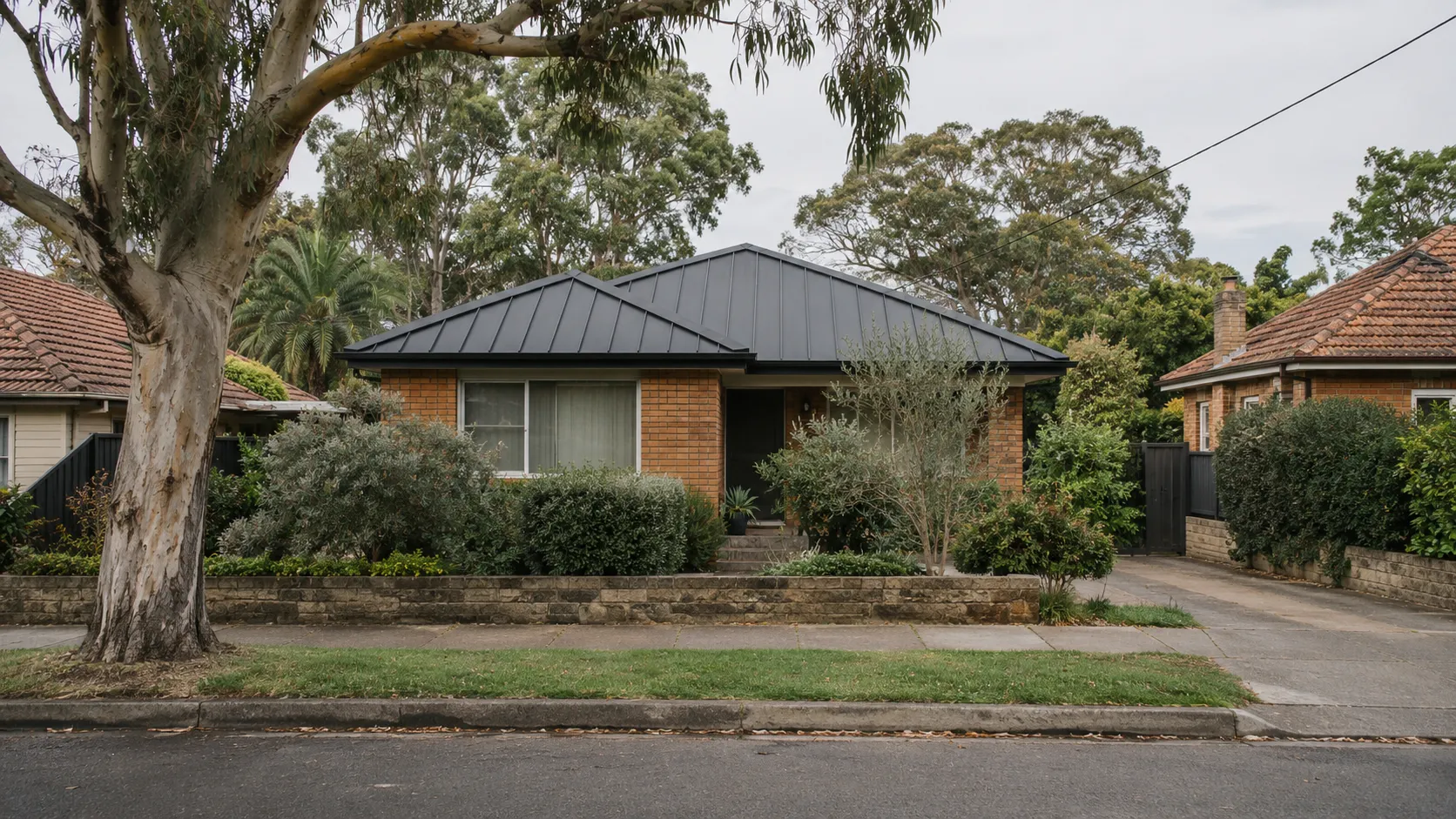 A brick bungalow with a dark standing-seam steel roof behind a low garden wall