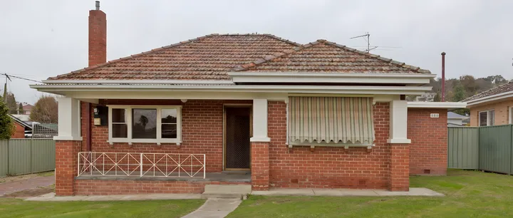 The same house before: red brick, a terracotta tile roof, a front verandah and a striped window awning