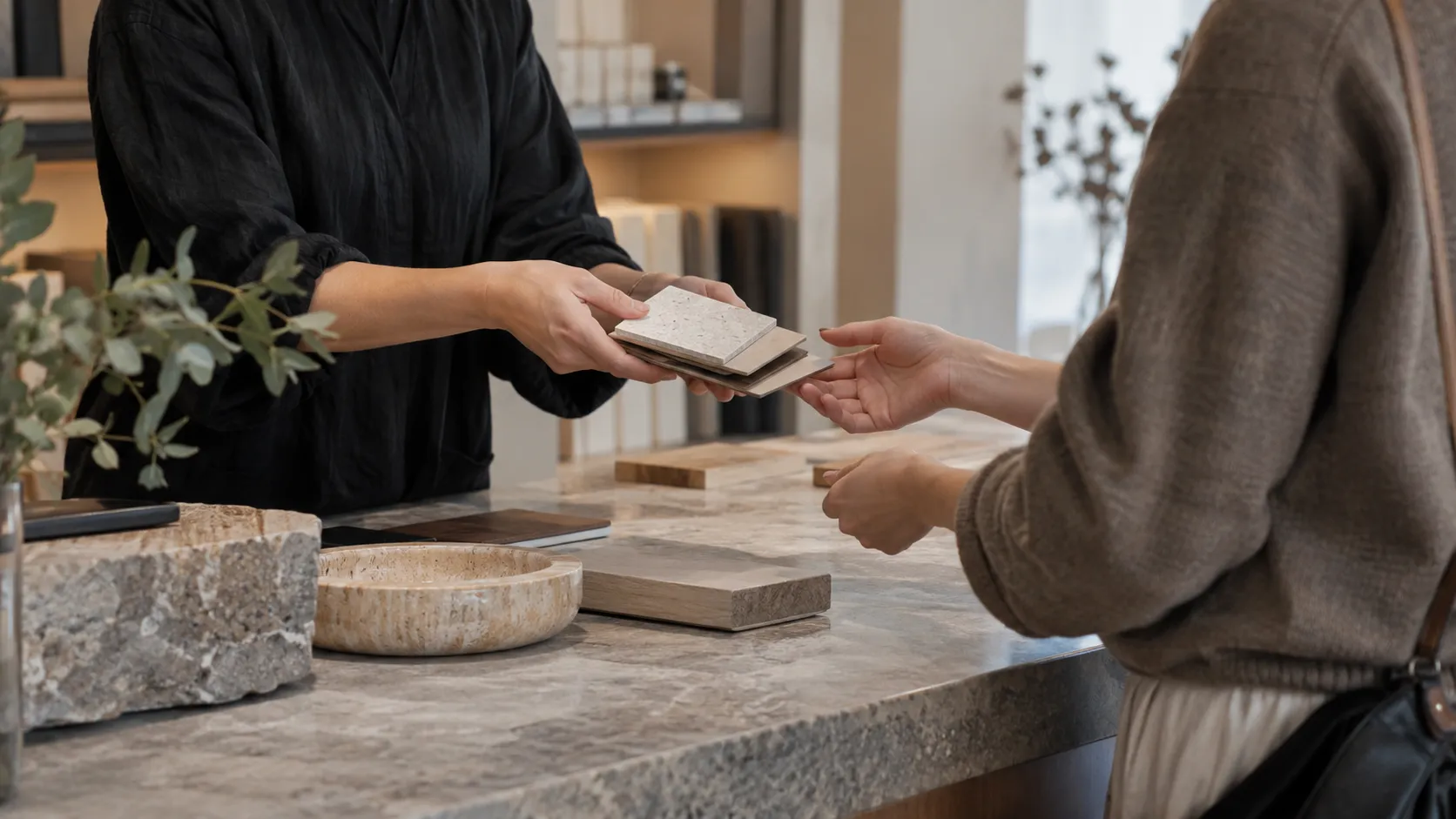 A shop assistant handing small stone and timber samples across a stone counter to a customer