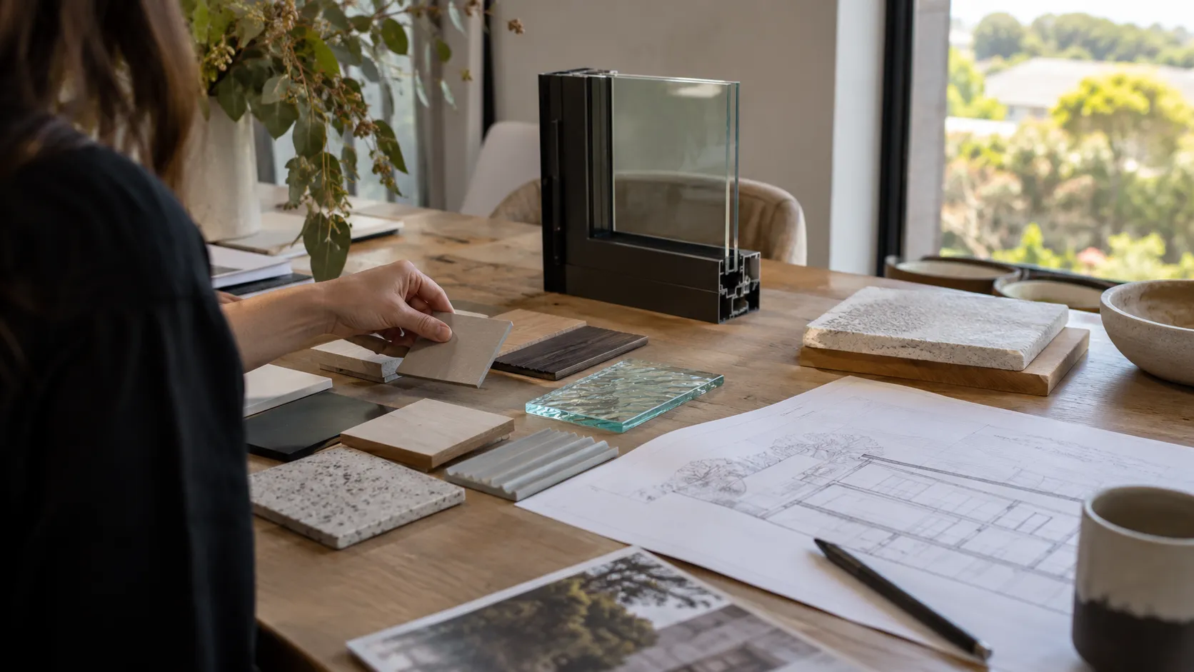 A designer’s table with a black window-frame corner section, glass sample, material swatches and plans