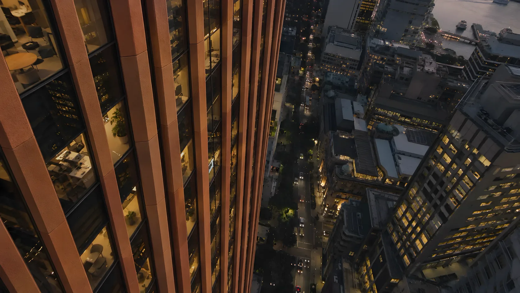 The same high-rise tower viewed from above at dusk, now with warm terracotta-coloured vertical facade fins and panels