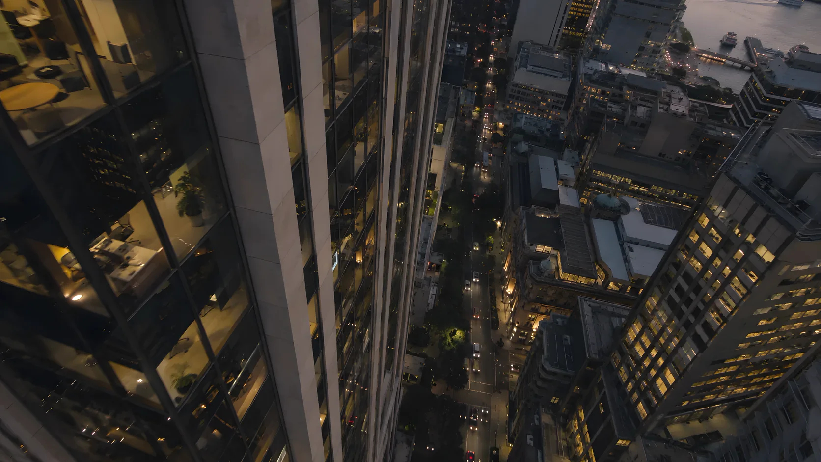 A high-rise glass and pale stone tower seen from above at dusk, with the lit city streets far below